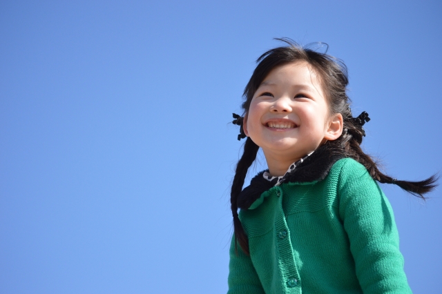 青空の下で笑顔を見せる緑の服の子ども