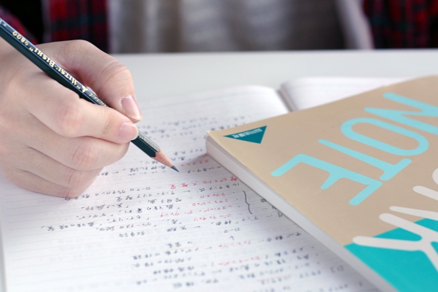 開いたノートに鉛筆で書き込む手元