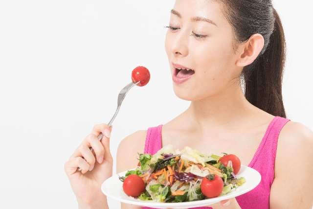 サラダのトマトを口へ運ぼうとする女性