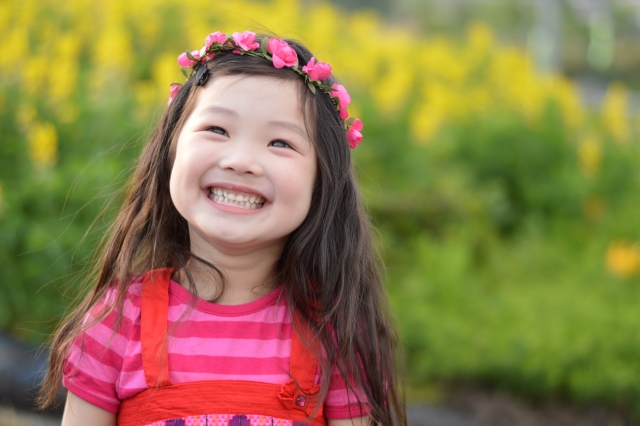 花冠をつけ、緑と黄色の花を背景に笑顔を見せる子ども