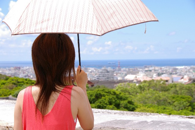 日傘を差して緑と海の見える風景を眺める女性の後ろ姿
