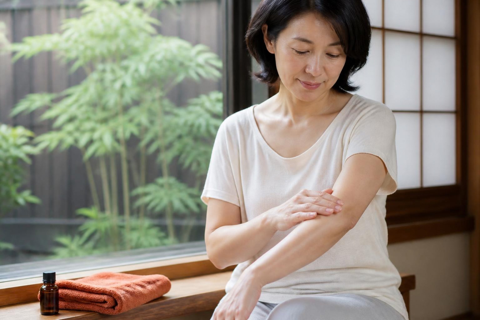 緑の庭に面した窓辺で腕にオイルをなじませる女性