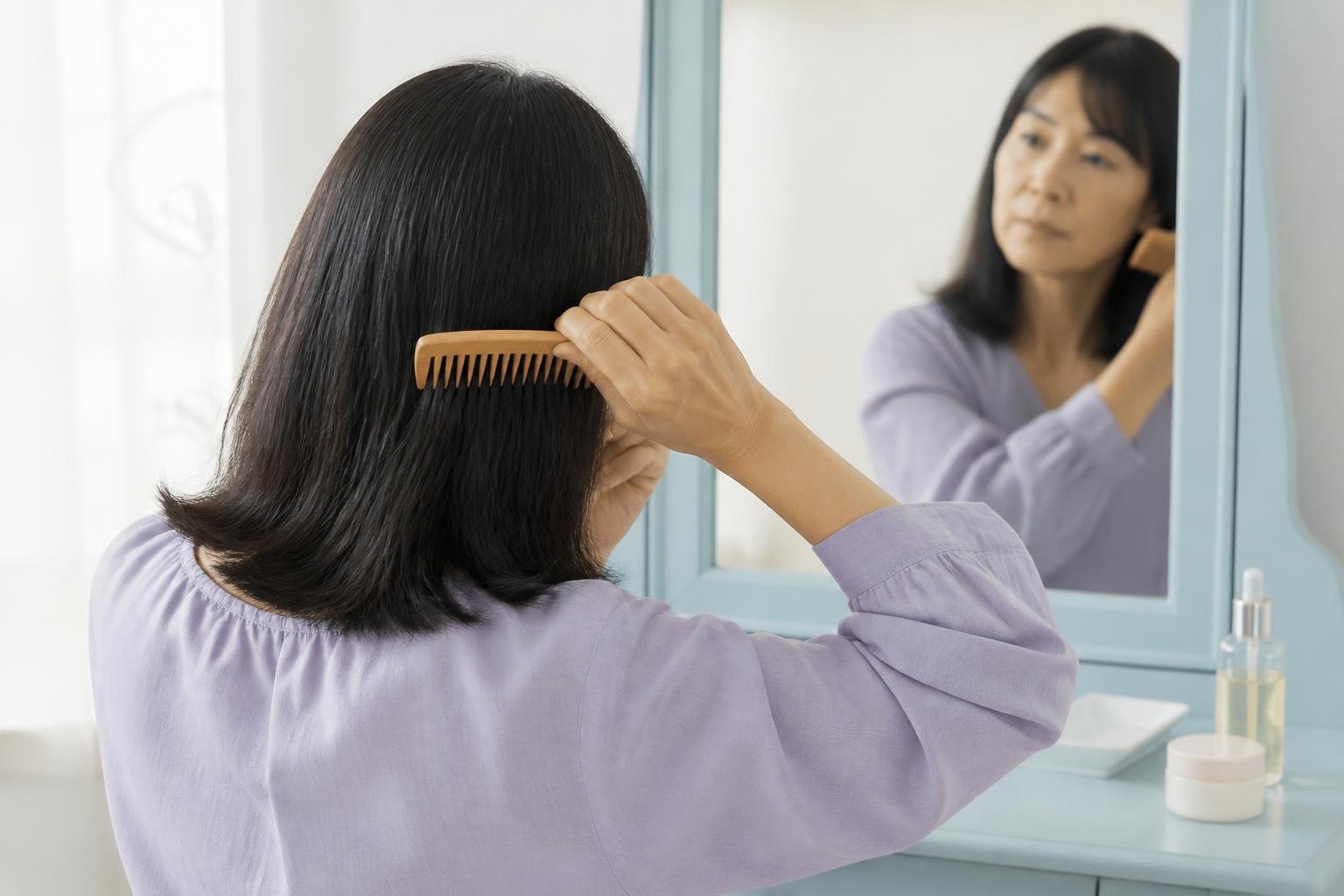 淡い紫の服を着た女性が水色の鏡台の前で髪をとかす