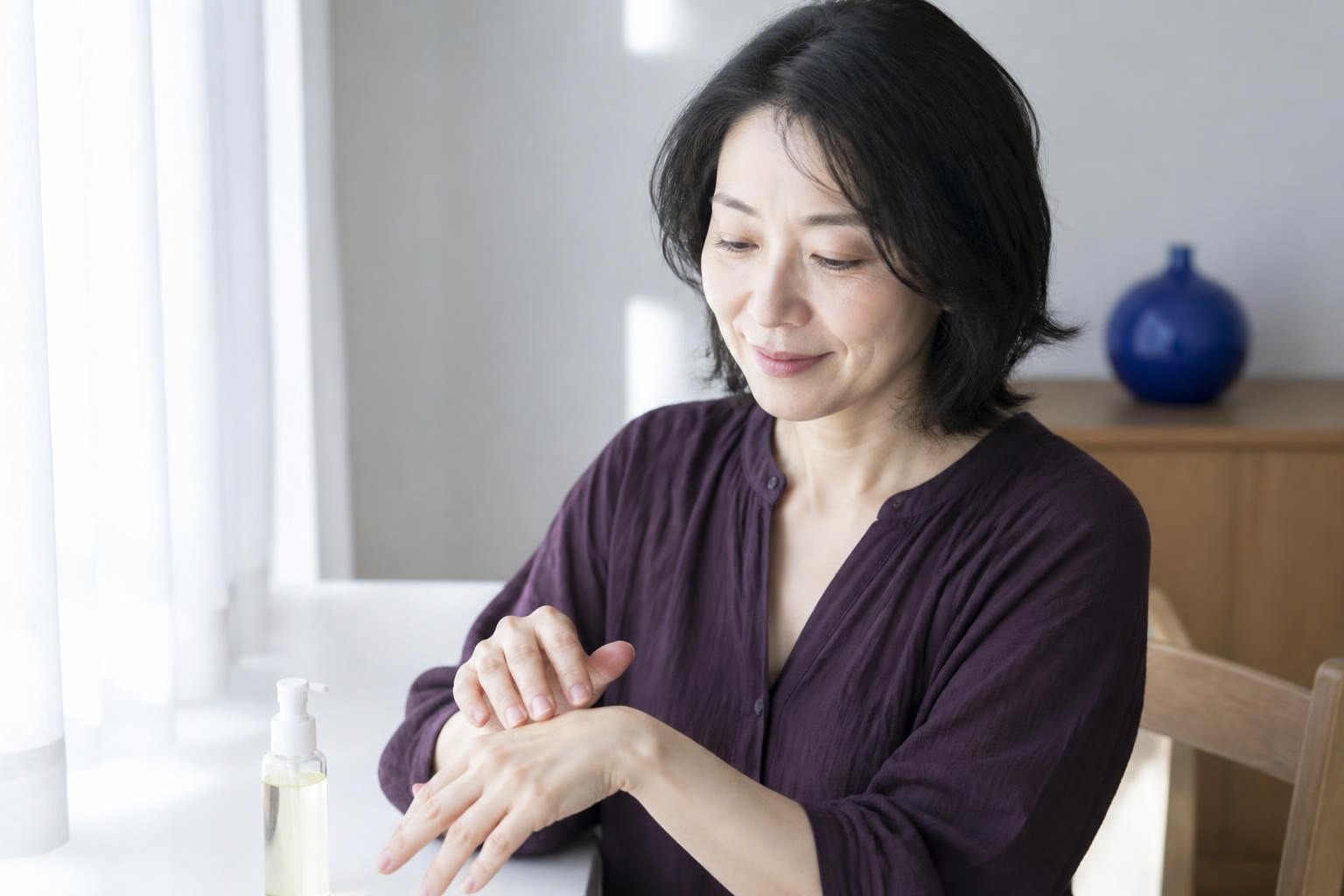明るい窓辺で手の甲をやさしくケアする紫色の服の女性