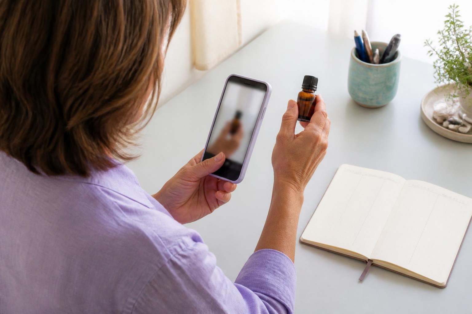小さな精油瓶をスマートフォンで撮影しノートに記録する女性