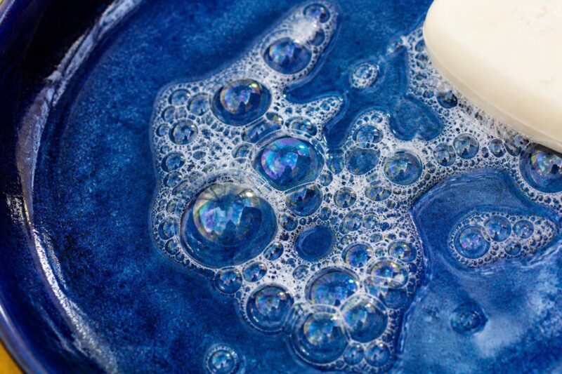 深い青の器に広がる、虹色の光を映した大小の石けんの泡