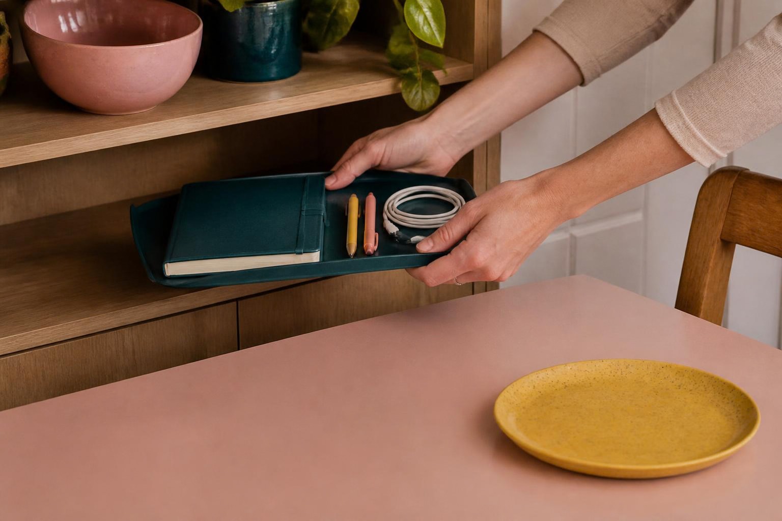 青緑のトレーにノートや充電器をまとめて棚へしまう手元