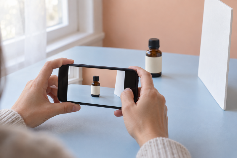 窓のそばで精油瓶をスマートフォンで撮影する手元